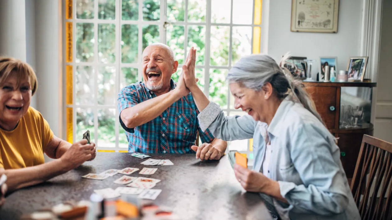 Seniors smiling and high-fiving as they play cards together., The Courtyards at Mountain View, Assisted Living in Denver, CO